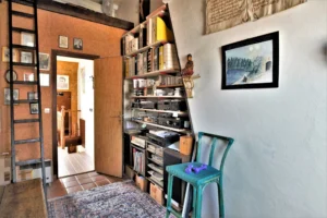 Espace sous combles d’un duplex rue du Faubourg Saint-Denis, avec bibliothèque remplie, échelle en bois, tapis persan et ouverture vers le palier.