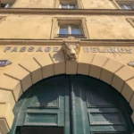 Entrée du Passage Delanos à Paris 10, montrant le porche voûté, la grande porte verte et l’emblème sculpté au-dessus de l’arche d’un immeuble de style haussmannien.