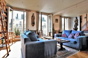 Séjour lumineux d’un duplex rue du Faubourg Saint-Denis, avec grandes fenêtres, parquet ancien, bibliothèque et décoration sculptée dans un appartement haussmannien à Paris 10.