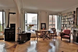 Séjour lumineux avec parquet en point de Hongrie, grande bibliothèque murale et coin repas, offrant une vue dégagée sur le square Alban Satragne depuis la rue du Faubourg Saint-Denis à Paris 10.