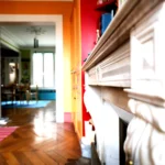 Détail d’une cheminée en pierre avec moulures, parquet en point de Hongrie et vue vers la salle à manger lumineuse d’un appartement situé rue du Faubourg Saint-Denis à Paris 10.