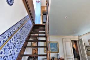 Escalier en bois menant à l’étage du duplex, avec murs décorés de carreaux bleus et éléments anciens dans un appartement situé rue du Faubourg Saint-Denis à Paris 10.