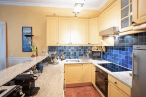 Cuisine aménagée avec meubles jaunes, plan de travail en pierre claire et crédence en carreaux bleu profond, dans un appartement situé rue de la Pompe à Paris 16.