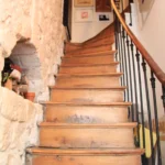 Escalier en bois ancien avec rampe en fer forgé, bordé d’un mur en pierre apparente dans un duplex du Passage Delanos à Paris 10.