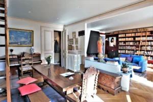 Grande pièce de vie d’un duplex rue du Faubourg Saint-Denis, avec bibliothèque murale, canapé bleu, table en bois massif et parquet ancien dans un appartement à Paris 10.