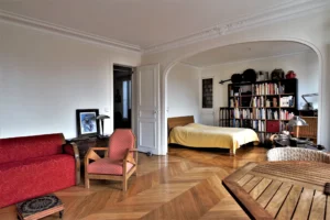 Grande pièce de vie avec parquet en point de Hongrie, alcôve aménagée en espace nuit, bibliothèque murale et mobilier ancien, dans un appartement situé rue du Faubourg Saint-Denis à Paris 10.