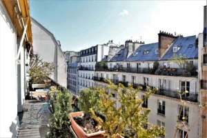 Balcon végétalisé d’un duplex rue du Faubourg Saint-Denis, avec table et chaises extérieures, offrant une vue dégagée sur les toits parisiens du 10ᵉ arrondissement.
