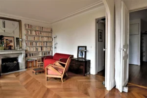 Espace salon avec bibliothèque murale, cheminée en marbre, parquet en point de Hongrie et mobilier ancien, dans un appartement situé rue du Faubourg Saint-Denis à Paris 10.