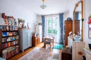 Chambre avec bibliothèque, parquet ancien, grande fenêtre donnant sur cour arborée et cheminée avec miroir doré, dans un appartement à Paris 16 rue de la Pompe.