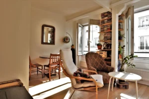 Salon lumineux d’un appartement rue Poissonnière Paris 2, avec fauteuils, table basse, plantes, bibliothèque et fenêtres ouvertes sur cour.