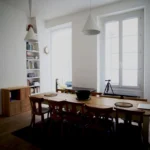 Salle à manger d’un appartement rue du Faubourg Saint-Denis à Paris 10, avec grande table en bois, étagères intégrées et fenêtre double vitrage.