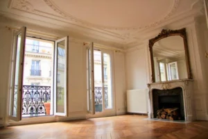 Salon haussmannien avec parquet point de Hongrie, cheminée en marbre surmontée d’un miroir ancien et grandes fenêtres ouvrant sur le balcon, rue Beaurepaire à Paris 10.