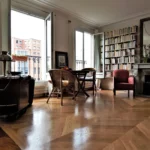 Salon lumineux avec parquet en pointe de Hongrie, grande bibliothèque murale et vue dégagée depuis les fenêtres donnant sur le Faubourg Saint-Denis à Paris 10.
