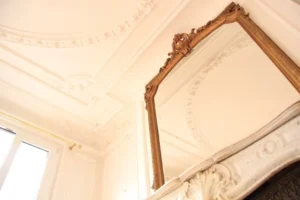 Détail des moulures haussmanniennes, du plafond orné et du miroir ancien surmontant la cheminée dans un appartement rue Beaurepaire à Paris 10.