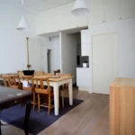 Salle à manger d’un appartement rue du Faubourg Saint-Denis à Paris 10, avec cuisine semi-ouverte, rangements en hauteur, table en bois et parquet clair.