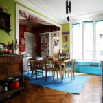 Salle à manger lumineuse avec grandes fenêtres, parquet en point de Hongrie, table en bois, moulures au plafond et alcôve décorative dans un appartement situé rue du Faubourg Saint-Denis à Paris 10.