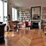 Salon lumineux avec parquet en pointe de Hongrie, grande bibliothèque murale et cheminée en marbre donnant sur la rue du Faubourg Saint-Denis à Paris 10.