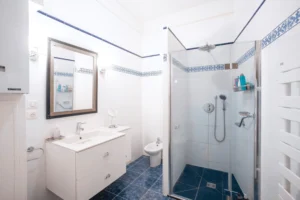Salle de bain avec cabine de douche vitrée, bidet, meuble vasque moderne et carrelage blanc et bleu, dans un appartement rue de la Pompe à Paris 16.