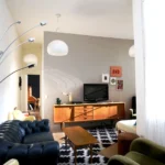 Salon lumineux d’un appartement rue du Faubourg Saint-Denis à Paris 10, avec meubles vintage en bois, canapé Chesterfield bleu, fauteuils rétro et grand tapis graphique.