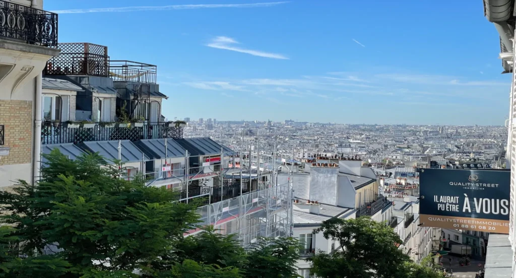 Vue panoramique sur Paris depuis Montmartre avec une campagne Quality Street Immobilier en premier plan — symbole du marché parisien en 2024 entre attractivité et réalignement.