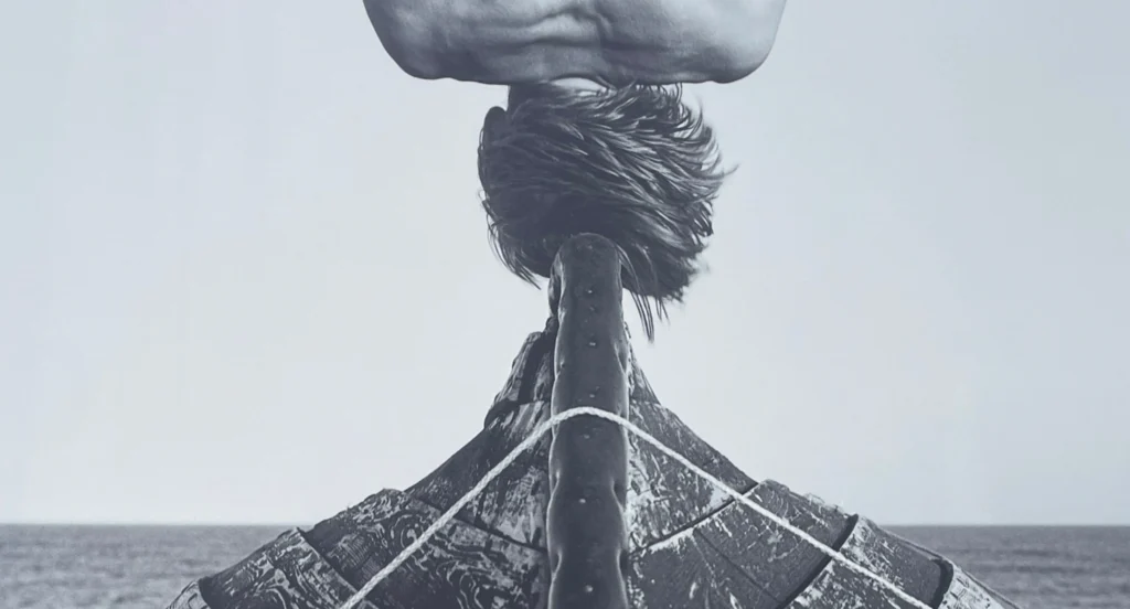 Photographie noir et blanc d’Arno Rafael Minkkinen à Deauville : corps penché au-dessus de la proue d’une barque face à la mer — festival Planches Contact Deauville