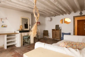 Séjour d’un appartement ancien à Paris 10, rue du Faubourg Saint-Martin, avec sol en tomettes, plafond à poutres apparentes blanchies, cheminée ancienne, mobilier vintage et lumière chaleureuse.