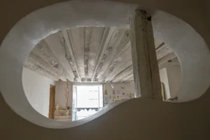 Ouverture architecturale organique donnant vue sur le séjour d’un appartement ancien à Paris 10, rue du Faubourg Saint-Martin, avec plafond à poutres apparentes blanchies et fenêtre sur rue.