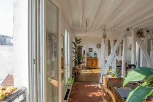 Couloir lumineux d’un duplex rue d’Aboukir, avec poutres apparentes, tomettes anciennes, plantes vertes et perspectives ouvertes sur les différentes pièces.