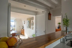 Vue depuis la cuisine d’un duplex rue d’Aboukir, avec plan de travail en bois, ouverture sur la salle à manger lumineuse et décoration murale élégante.