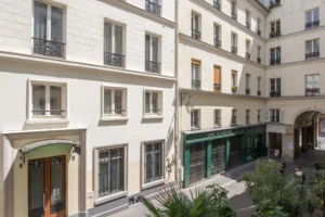 Vue sur la rue dans le 10e arrondissement de Paris, quartier Faubourg Saint-Martin, avec immeubles anciens, façades claires, garde-corps en fer forgé et vie de quartier au pied de l’immeuble.