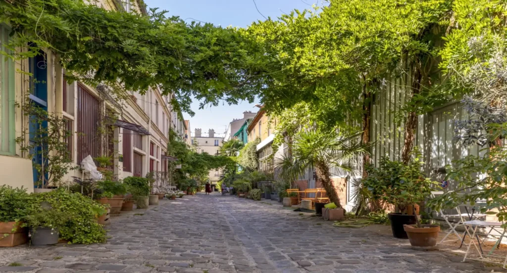 Copropriété végétalisée dans un passage pavé à Paris — façades d’ateliers et appartements bordés de plantes, ambiance calme et verdoyante illustrant un cadre de vie apaisé.