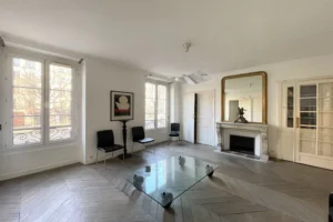 Salon d’un appartement à vendre à Paris 11, boulevard du Temple, avec parquet en point de Hongrie, cheminée ancienne, grandes fenêtres et vue dégagée.