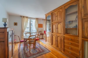 Séjour avec espace salle à manger d’un appartement à vendre à Paris 12 Picpus, parquet en bois, mobilier ancien, grande armoire, table ronde, double fenêtre et lumière naturelle.