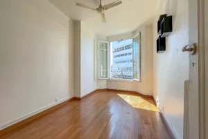 Séjour avec parquet en bois, murs blancs, fenêtre à battants ouverte laissant entrer la lumière, ventilateur au plafond, dans un appartement à Paris 12 Reuilly-Diderot.