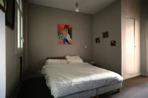 Chambre d’un appartement ancien à vendre à Paris 16 Molitor, lit double, parquet au sol, placards intégrés, murs peints et fenêtre apportant une ambiance calme.