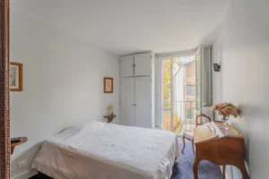 Chambre d’un appartement à vendre à Paris 12 Picpus avec placards intégrés, parquet au sol, lit double, petit bureau, porte-fenêtre et vue dégagée sur l’extérieur.