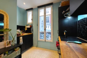 Cuisine équipée d’un appartement à vendre à Paris 18 Place de Clichy, avec plan de travail en bois, crédence noire, rangements fonctionnels, fenêtre sur rue apportant une belle luminosité et ambiance contemporaine.