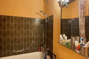 Salle de bains d’un appartement à Paris 17 Pont Cardinet avec baignoire, douche, miroir mural et carrelage d’époque.