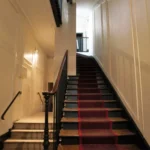 Cage d’escalier d’un immeuble ancien à Paris 5, quartier des Gobelins, avec escalier en bois, rampe en ferronnerie et tapis central, parties communes soignées.