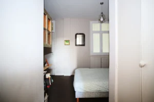 Chambre secondaire d’un appartement ancien à vendre à Paris 16 Molitor, lit simple, rangements intégrés, étagères murales, fenêtre en hauteur et atmosphère calme.
