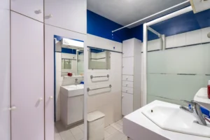 Salle de bains d’un appartement à vendre à Paris 12 Picpus, baignoire avec paroi vitrée, meuble vasque, miroir, nombreux rangements intégrés, carrelage blanc et espace fonctionnel.