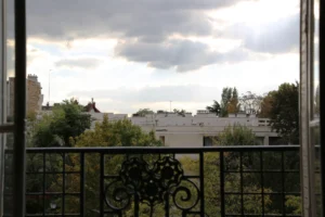 Vue depuis le balcon d’un appartement à vendre à Paris 16 Molitor, garde-corps en fer forgé, perspective dégagée sur les toits et les arbres, environnement calme et résidentiel.