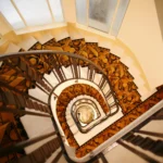 Cage d’escalier d’un immeuble ancien à Paris 16 Molitor, escalier tournant en pierre, rampe en métal, tapis graphique et verrière apportant de la lumière naturelle.