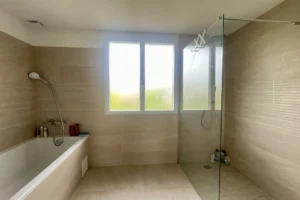 Salle de bain avec baignoire, douche à l’italienne et fenêtre apportant une belle lumière naturelle, maison à vendre à Saint-Benoît-d’Hébertot.