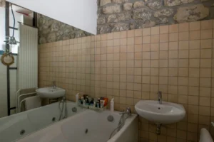 Salle de bains avec baignoire balnéo, double vasque et murs en pierre apparente dans un appartement de caractère à Paris 10.