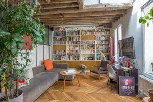 Salon avec bibliothèque sur mesure toute hauteur, parquet en point de Hongrie, espace bureau et poutres apparentes dans un appartement de caractère à Paris 10.