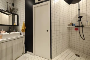 Douche à l’italienne dans la salle d’eau d’un appartement à vendre à Paris 18 Place de Clichy, avec carrelage blanc contemporain, robinetterie noire, receveur de plain-pied et espace bain fonctionnel.