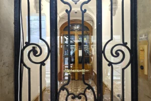 Entrée d’un bel immeuble ancien à Paris 18 Place de Clichy, avec porte vitrée, ferronneries d’époque, parties communes soignées et accès sécurisé depuis la rue.