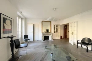 Séjour d’un appartement à vendre à Paris 11, secteur Filles du Calvaire, avec cheminée ancienne, grand miroir doré, parquet en point de Hongrie et portes vitrées.