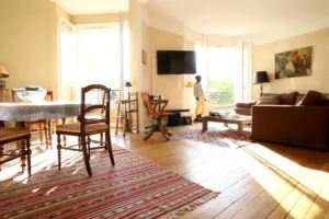 Séjour et salle à manger d’un appartement ancien à vendre à Paris 16 Molitor, parquet d’origine, espace de réception ouvrant sur balcon, mobilier classique, vue arborée et ambiance calme.